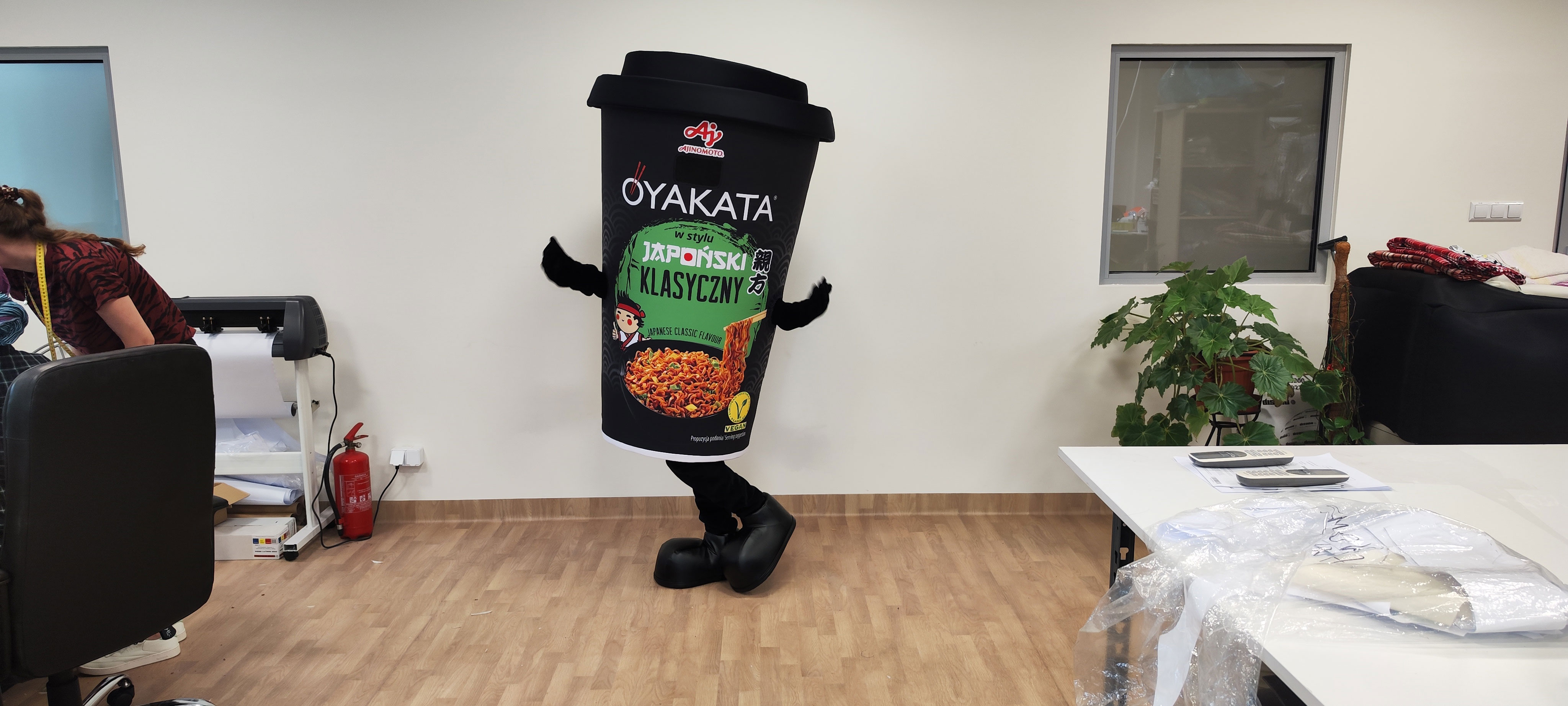 Na fotografii widnieje kostium reklamowy w postaci kubka pozujący do zdjęcia w siedzibie firmy Elabika
